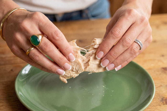 Hand breaking a fresh piece of light beige ginger root over a green ceramic plate on a wooden table.
