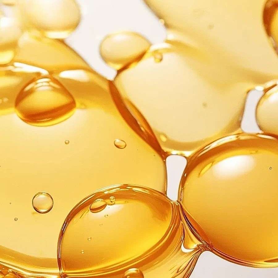 Amber-colored liquid droplets on a light background, showcasing a glossy and viscous texture. Ideal for skincare products.
